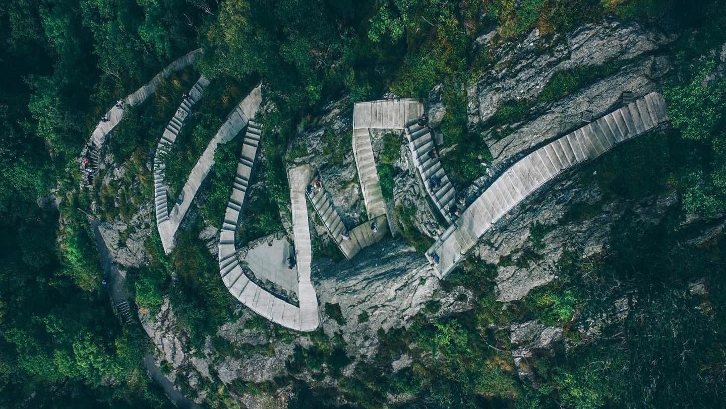 Vista aérea de un sendero de escaleras que zigzaguea y asciende por una montaña cubierta de bosque