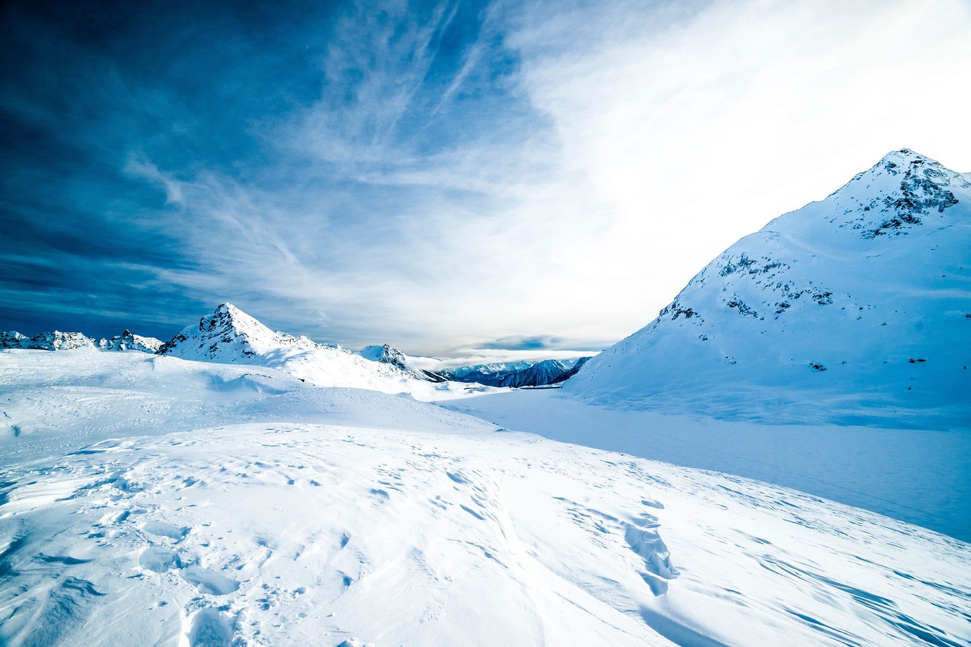 Paisaje de montañas nevadas bajo un cielo azul con nubes